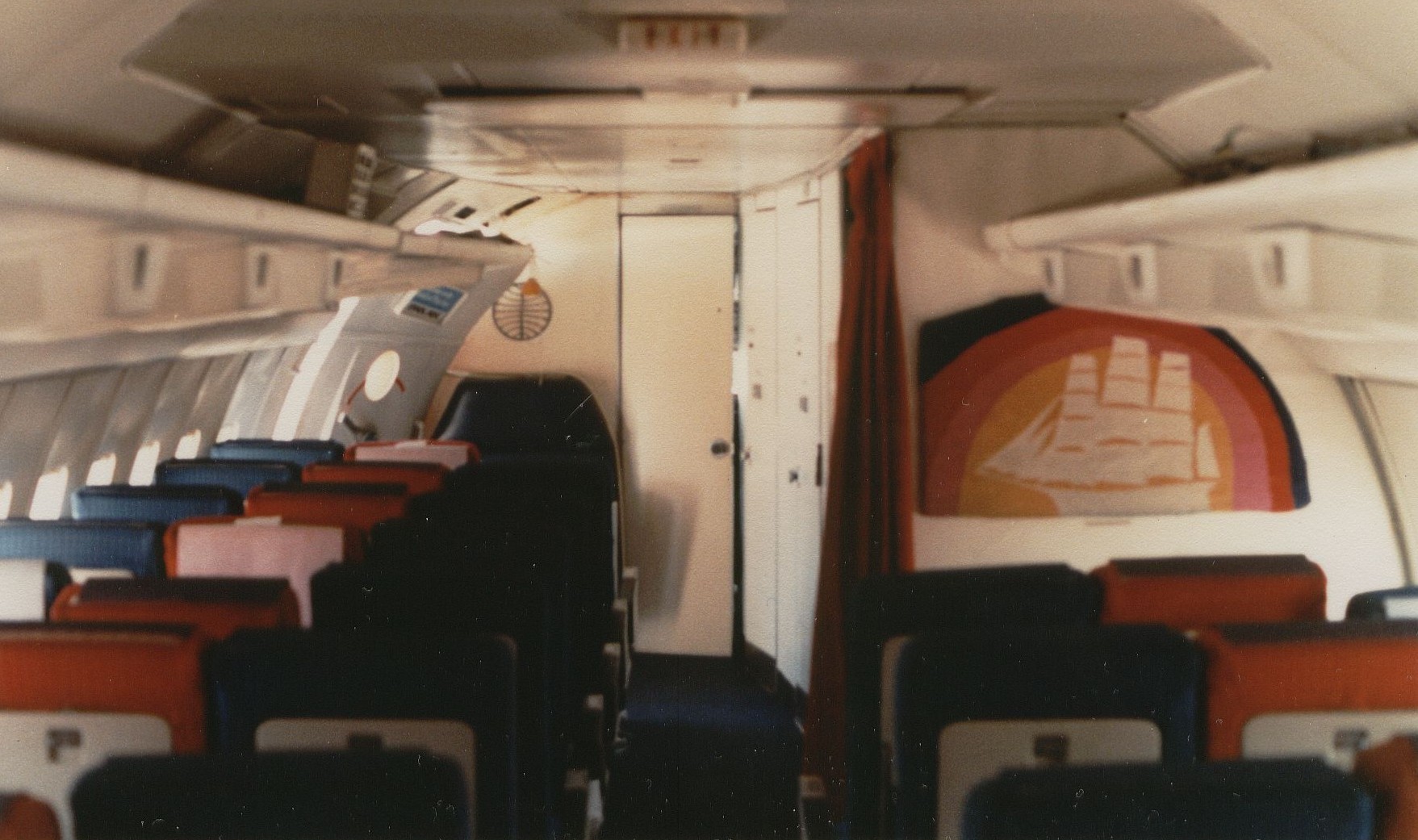August 1981 The forward cabin of a Pan Am Boeing 707 in an all economy configuration with 180 seats.  In front of the Clipper Ship bulkhead artwork is the forward galley and two lavatories.  In the front center isthe door to the cockpit and to the left the passenger door.